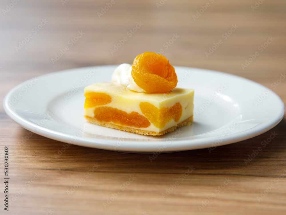 Delicious dried apricot mousse cake slice with white chocolate cream on top on wooden table background. Restaurant menu and confectionery concept. Close-up. Copy space. Delicious dried apricot mousse cake slice with white chocolate cream on top on wooden table background. Restaurant menu and confectionery concept. Close-up. Copy space.