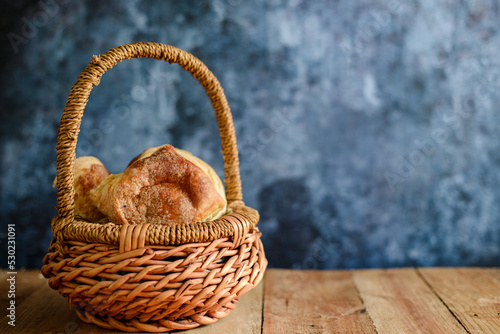 Wicker basket with sweet breads on wooden table. Blue background.