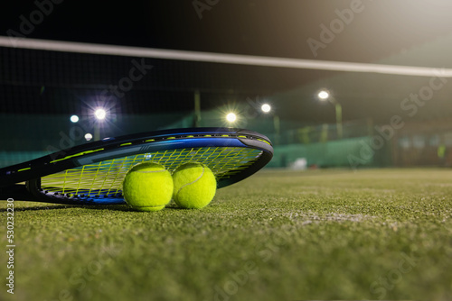 play tennis in dark with artificial lighting. racket and balls on outdoor court with copy space © ronstik