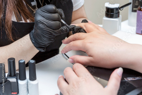 Manicure procedure in a beauty salon. Master in black gloves and the hands of the client. Personal care and cosmetics. Close-up.