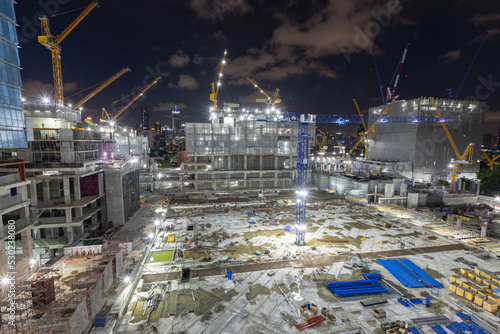 Aerial view of a large construction of a residential area with many multi-storey buildings under construction, a lot of tower cranes, workers, construction equipment at sunset