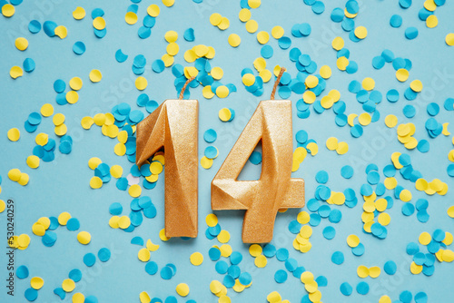 Number 14 fourteen golden celebration birthday candle on yellow and blue confetti Background. fourteen years birthday. concept of celebrating birthday, anniversary, important date, holiday