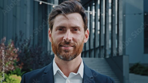 Handsome bearded caucasian man looking away turns to camera close-up successful professional manager leader businessman in suit standing outdoors smiling confident male entrepreneur posing on street