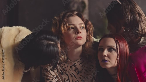 Slowmo of eccentric team of glamorously dressed vogue dancers looking seductively at camera and making tempting movements with their arms, dancing together in dark studio