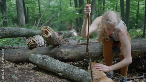 a blonde woman sitting on a fallen tree in the forest, petting the dog Shiba Inu