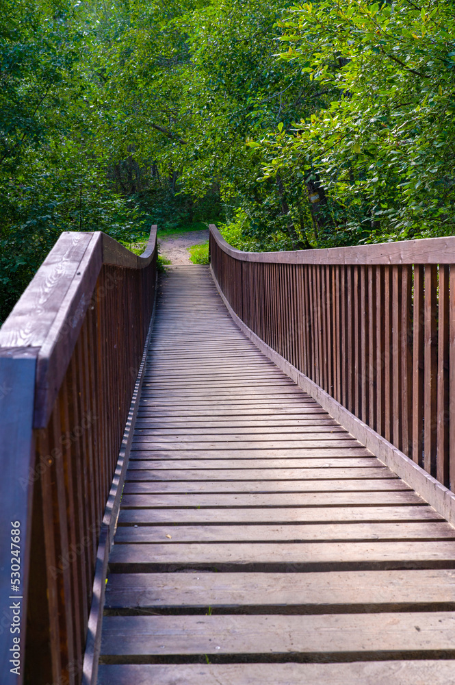 Wooden narrow bridge with high railings across a small river