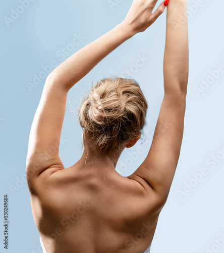 Naked female raised arms stretching her back muscles, rear view. Advertising of massage and spa treatment procedure, cosmetics for body care. Healthy spine and posture, woman's wellness concept.