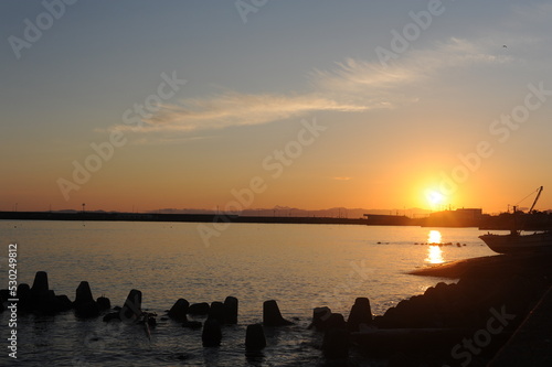 Sunset with a clear sky and sunlight reflexing on the surface of an ocean in the evening at the beach at the sea in fishing town in summer in Japan