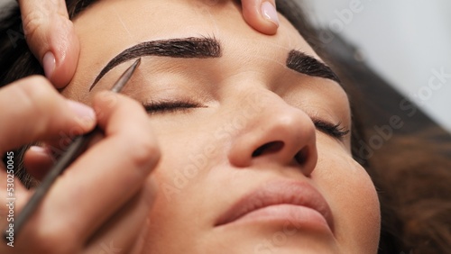 Woman is  on the Eyebrow coloring procedure. Professional lamination procedures of female eyebrows in beauty salon. Closeup view of client face and stylist's hands working.  Beauty care concept. photo