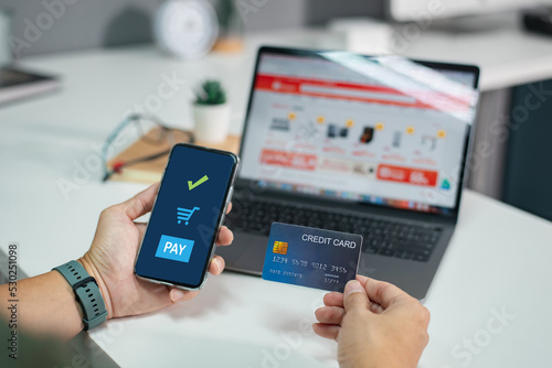 Online shopping concept, young man hands holding mobile smart phone showing payment success on screen and credit card with laptop on table while sitting in office, lifestyles technology