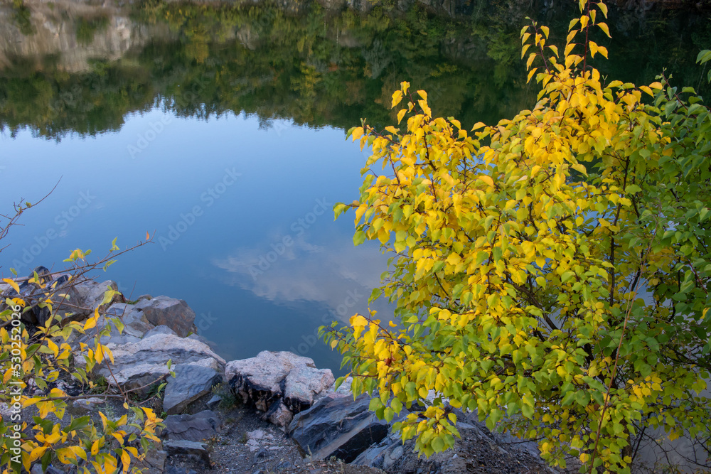 Landscape with lake, trees, and rocks in autumn. Trees reflected in water. Tree with yellow leaves on lake background Landscape with lake, trees, and rocks in autumn. Trees reflected in water. Tree with yellow leaves on lake background