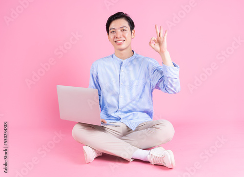 Young Asian man sitting and using laptop on background