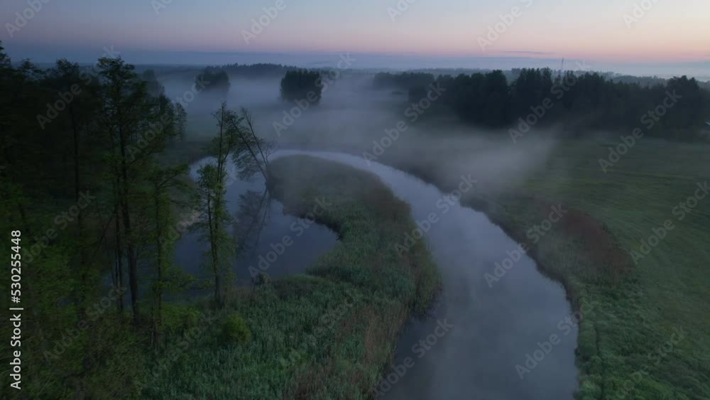 Slow drone flight over the green field, forest and narrow river. Foggy morning. Slow drone flight over the green field, forest and narrow river. Foggy morning.