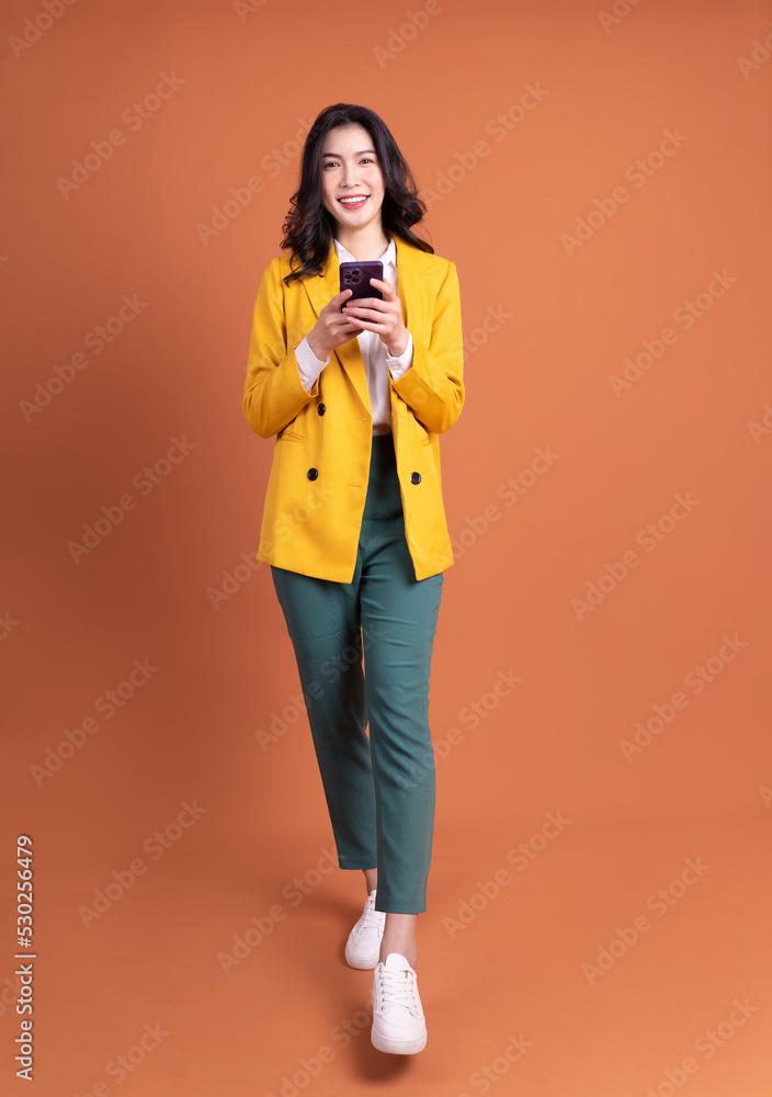 Full length image of young Asian woman using smartphone on background Full length image of young Asian woman using smartphone on background