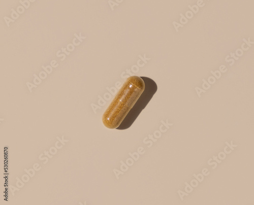 Brown Medical capsule on light beige top view, hard shadows. Taking dietary supplements