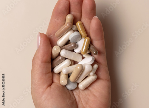 Hand with mix of medical capsules on light beige top view. Taking dietary supplements