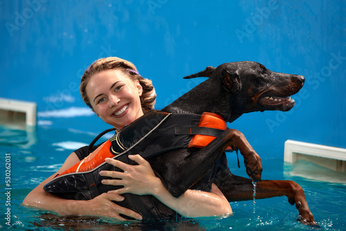 Schilderij op canvas Dog in life jacket swim in the swimming pool with coach