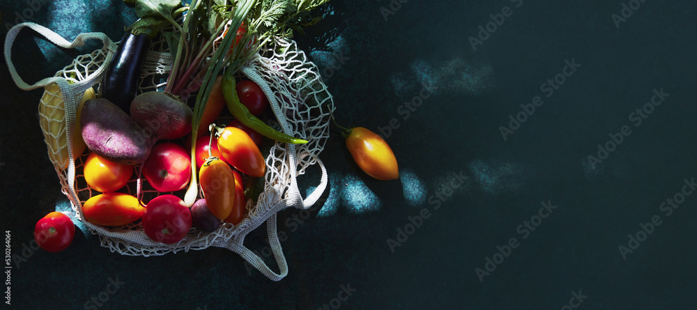 Fresh vegetables - yellow tomatoes, eggplant, onion, beetroot in eco shopping bag under trendy hard shadows with reflection background. Ecological concern. Copy space. Extra wide banner