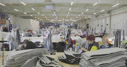 Many seamstresses work in a garment factory. Working process at a garment factory. Large sewing workshop. Seamstresses make products in a factory. Garment factory