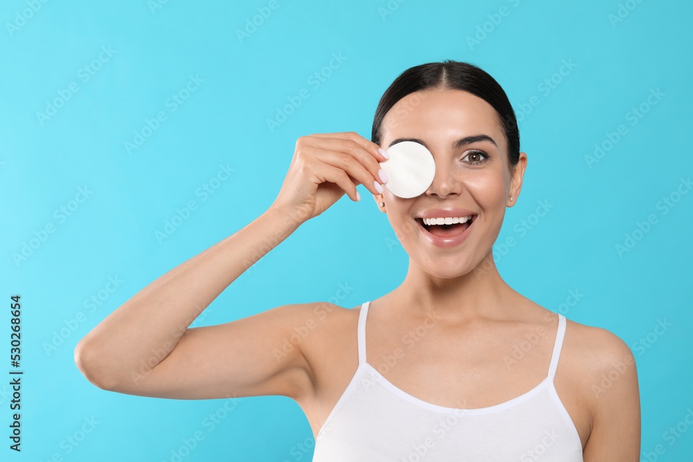 Young woman using cotton pad with micellar water on light blue background Young woman using cotton pad with micellar water on light blue background