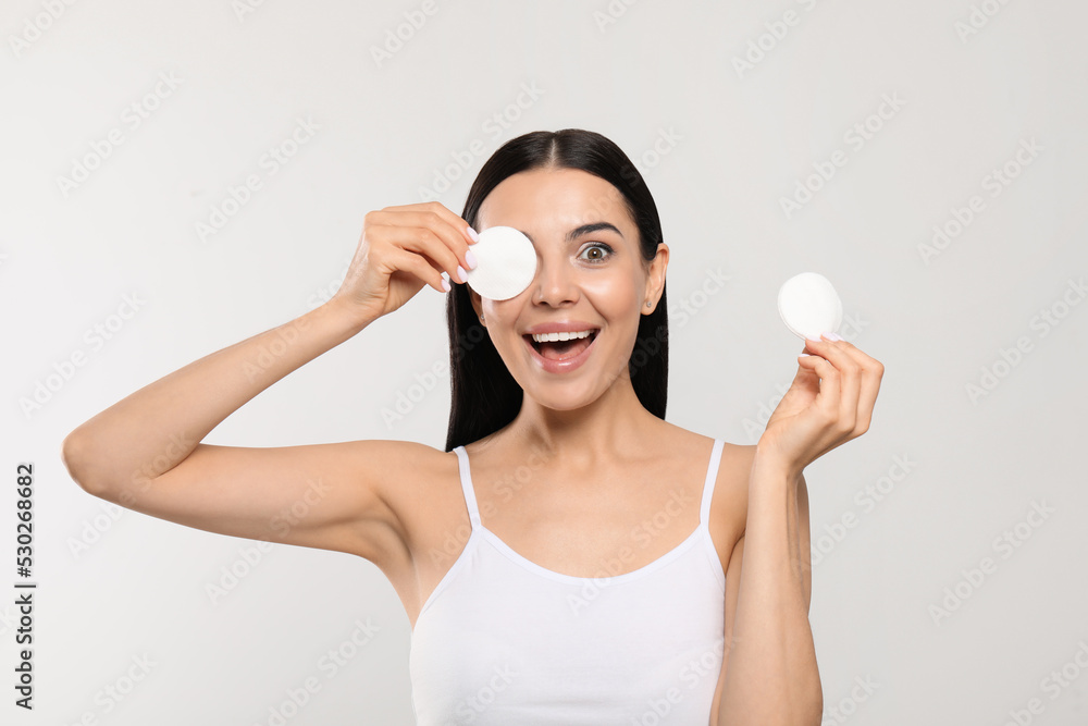Young woman using cotton pads with micellar water on light grey background Young woman using cotton pads with micellar water on light grey background