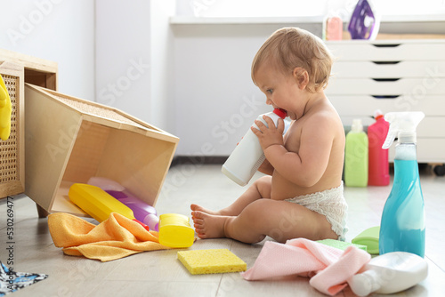 Cute baby playing with bottle of detergent on floor at home. Dangerous situation photo