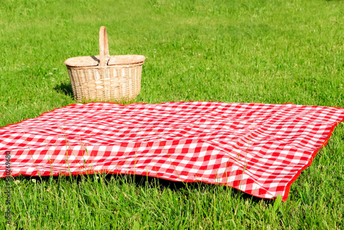Checkered tablecloth and picnic basket on green grass