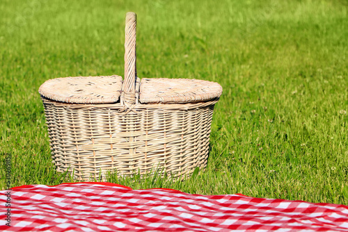 Fototapeta Naklejka Na Ścianę i Meble -  Picnic basket and checkered tablecloth on green grass outdoors