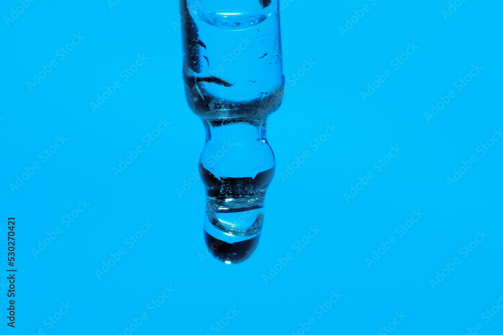 Dripping face serum from pipette on blue background, closeup Dripping face serum from pipette on blue background, closeup