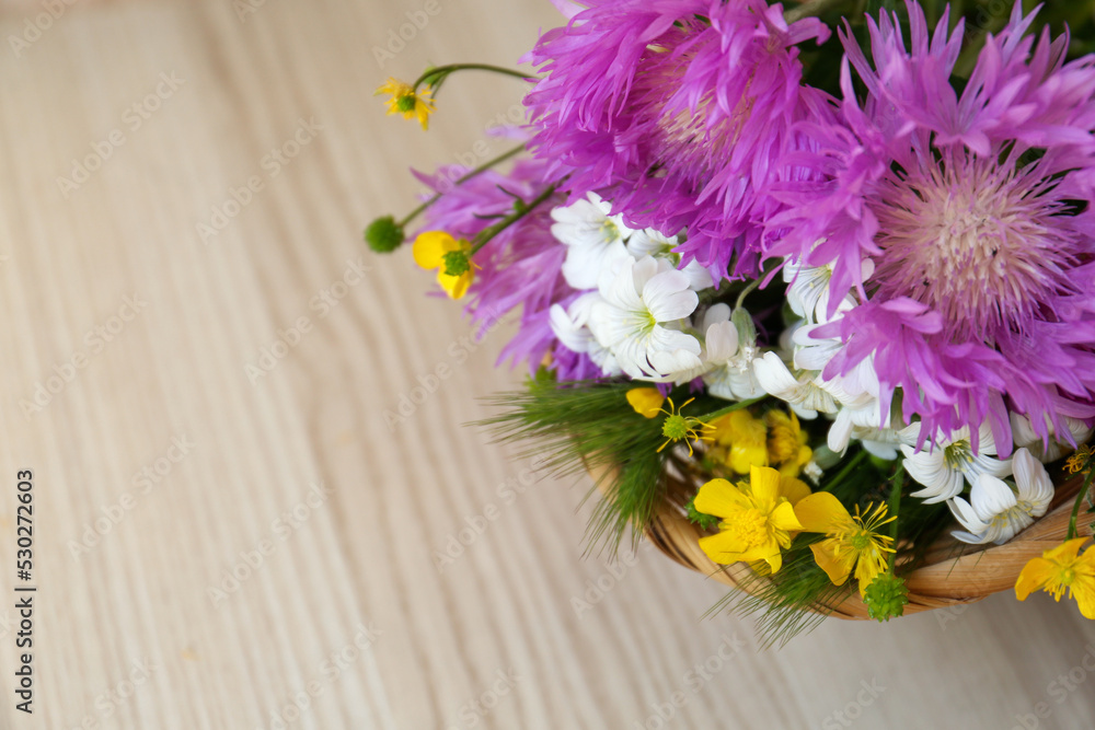 Bouquet of beautiful wildflowers in wicker basket on wooden table, above view. Space for text