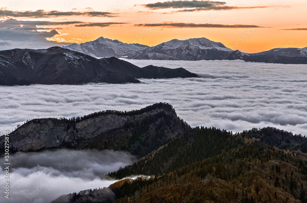 Beautiful scenic dramatic autumn sunset landscape of mountain valley covered with shroud of low clouds viewed from top of Maliy Tkhach mountain peak in West Caucasus, Russia.