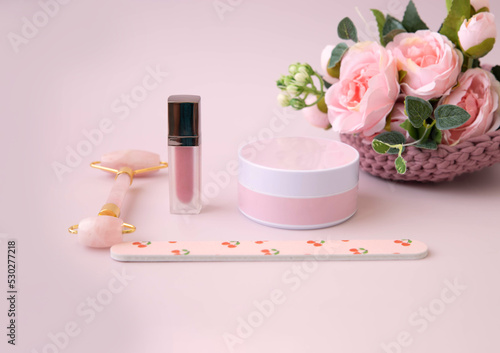 On a pink background, a jar of cream, a facial massager, flowers, a nail file, a shopping list