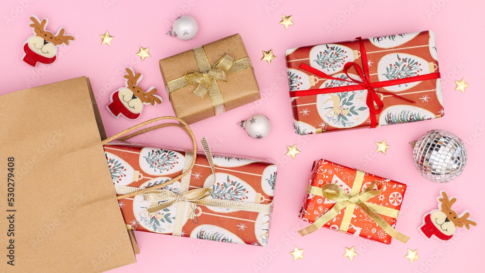 Fototapeta premium Christmas gifts with ribbons in eco friendly shopping bag on pastel pink background. Flat lay