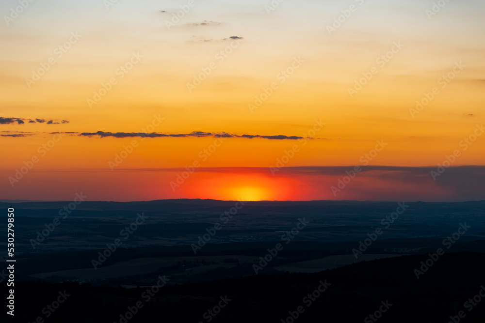 Landscape with sun, glowing sky and clouds. The sun is low, just before setting. View from Feldberg mountain in Hesse, Germany.