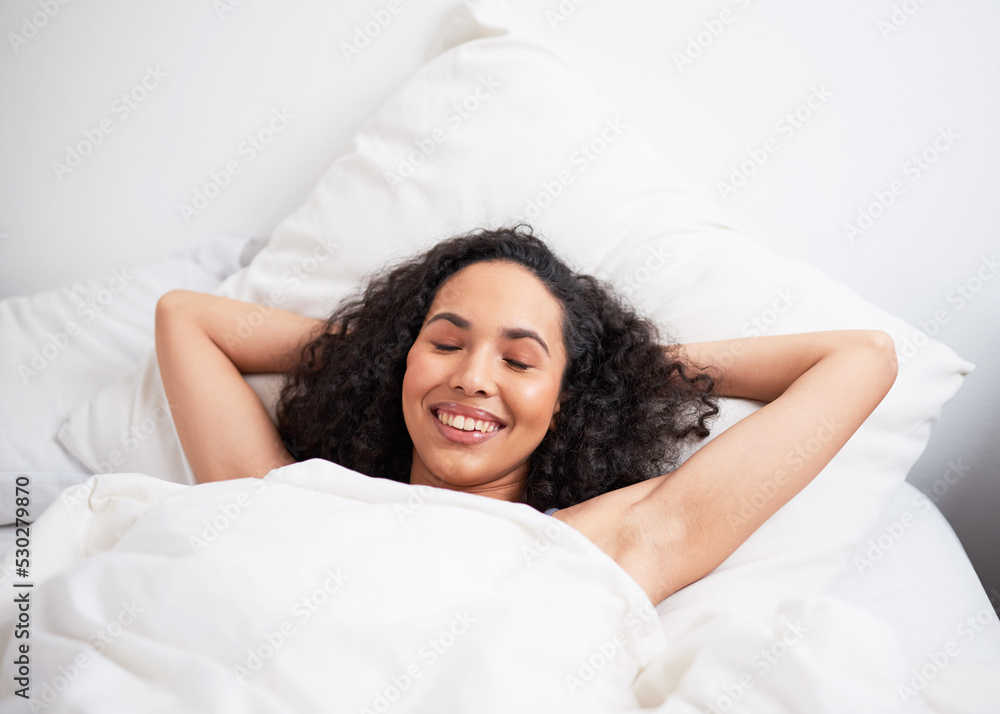 A young biracial woman lies in bed with arms behind head and eyes closed resting A young biracial woman lies in bed with arms behind head and eyes closed resting