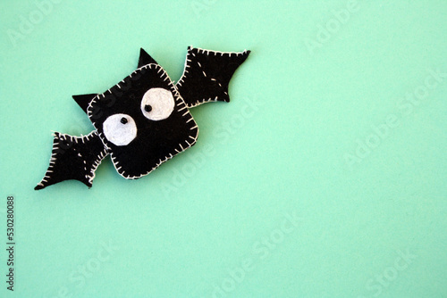 A black bat sewn from felt on a green background. A toy for Halloween.