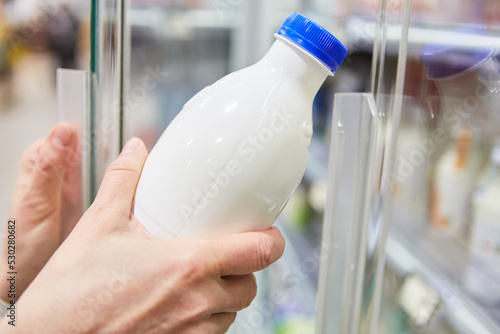 Hand hält eine Flasche mit veganer Milch am Kühlregal photo