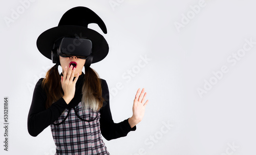 Metaverse concept, halloween theme, young asian girl in witches costume wearing witch hat and vr headset posing watching playing and exciting on white background. 