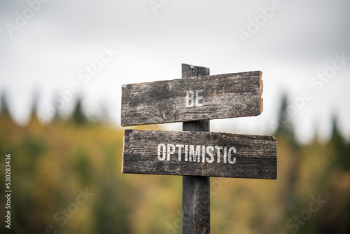 Foto vintage and rustic wooden signpost with the weathered text quote be optimistic, outdoors in nature