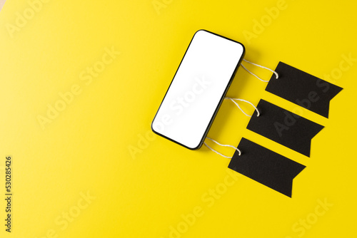 Composition of smartphone with gift tags on yellow background