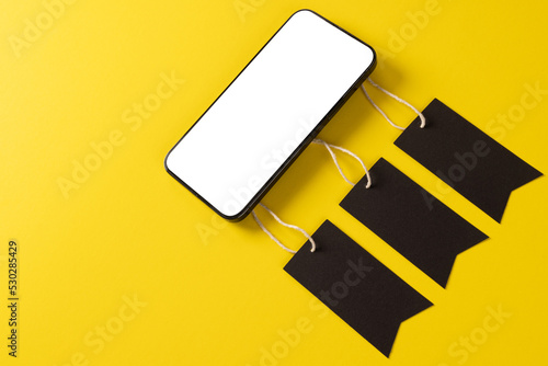 Composition of smartphone with gift tags on yellow background