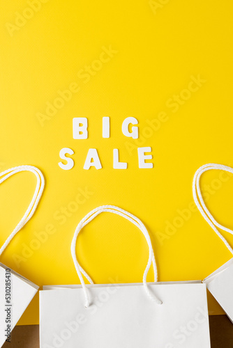 Composition of paper bags and big sale text on yellow background