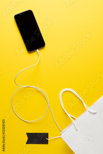 Composition of smartphone with gift tag and bag on yellow background