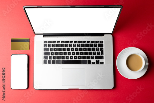 Composition of cup of coffee, smartphone and laptop with copy space on pink background