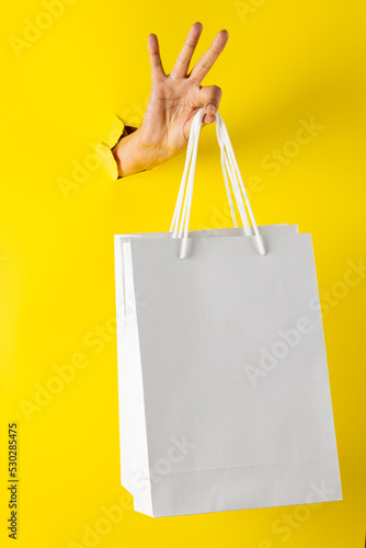 Composition of hand holding shopping bags on yellow background