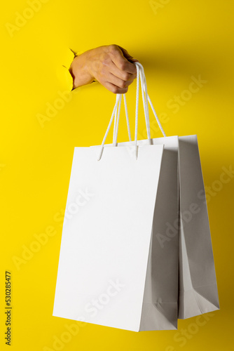 Composition of hand holding shopping bags on yellow background