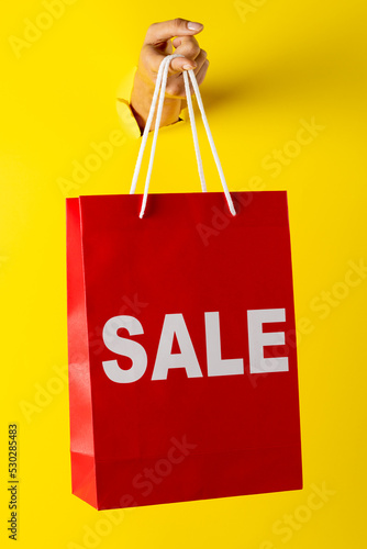 Composition of hand holding shopping bag with sale text on yellow background