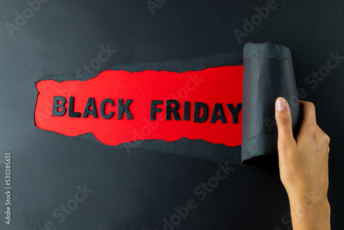 Composition of hand with black paper and black friday text on red background