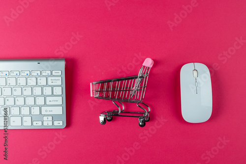 Composition of keyboard, mouse and shopping cart on pink background