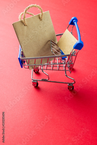 Composition of shopping cart with bag and copy space on pink background